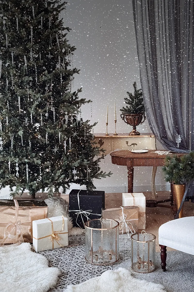Christmas tree with icicle ornaments, wrapped gifts, glass lanterns and grey curtains in a festive set at Luma Studio Dubai.